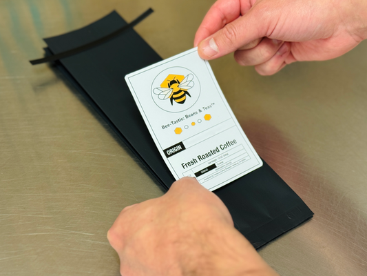Bee-Tastic: Beans & Teas™ being labeled by a pair of hands.