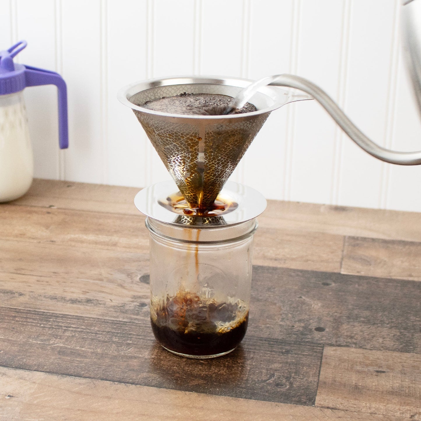 Coffee being poured through a filter into a glass jar on a wooden surface.